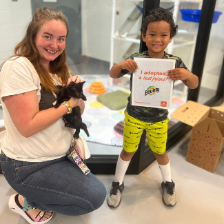 Woman holding kitten next to little boy holding adoption event sign