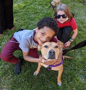 Two young kids in grass with one hugging tan dog