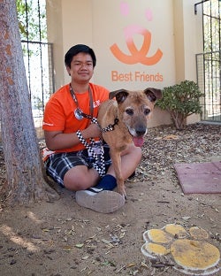 Young man in orange shirt in sitting in front of BF building with brown dog