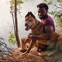 Man and brown dog sitting on edge of stream