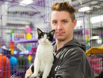 Man holding black and white cat in front of cage