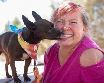 Adopter in pink shirt with small dog kissing her face