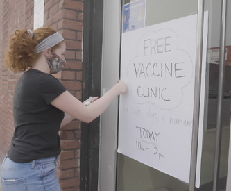 Woman with hair in ponytail hanging up vaccine clinic sign