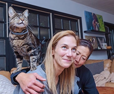 Two women sitting on couch with cat on one's shoulder