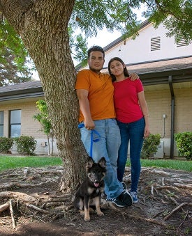 Man and woman standing in front of tree with black and brown German shepherd puppy