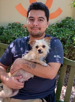 Man in dark tshirt holding small tan dog
