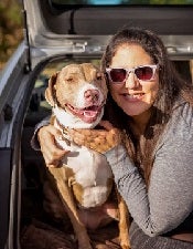 Lady in sunglasses sitting with dog in back hatch of car