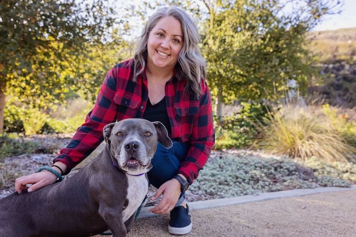 A woman poses for the camera with an older gray dog