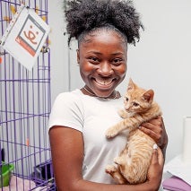 Young woman holding orange kitten in front of cat cage