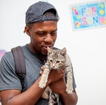 Man in gray hat and shirt holding tabby kitten