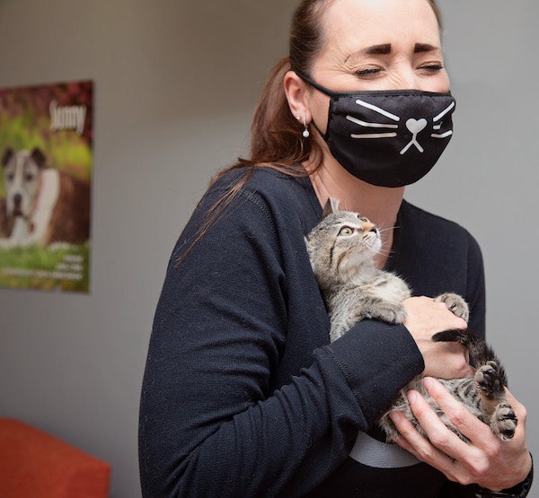 A person wearing a facemask holding a kitten