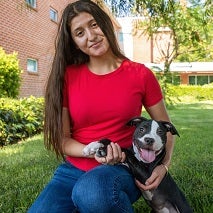 Woman with long dark hair in red shirt holding black and white puppy