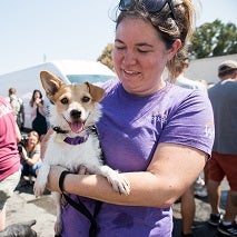 Woman in purple shirt holding tan and white dog
