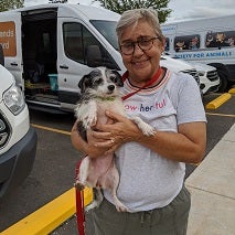 Woman in white t-shirt holding small black and white dog in front of transport van
