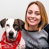 Kristan McCormick in a Save Them All sweatshirt pictured with a brown and white mixed breed dog wearing a bandana and being a good boy