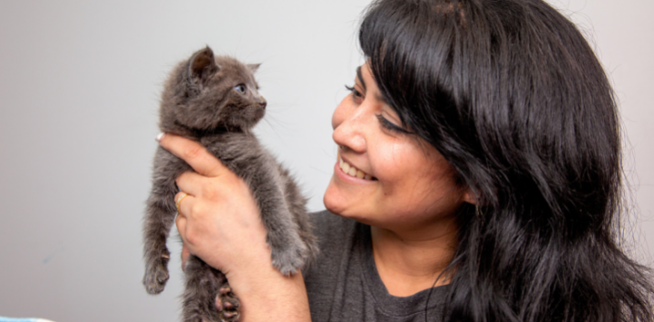 Woman with dark hair holding dark gray kitten to her face