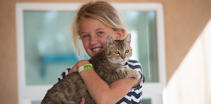 Young girl in black and white top holding tabby cat.