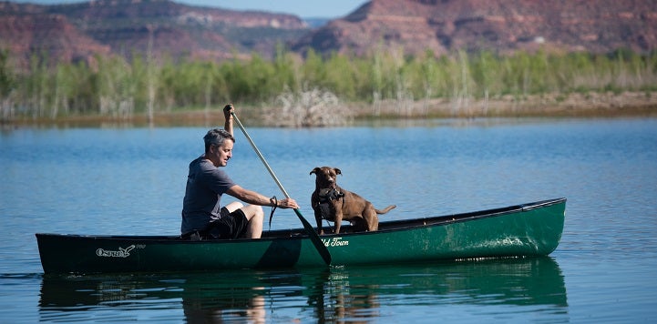 Man and dog in green canoe on water with mountains in background