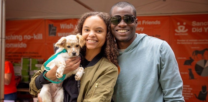 Man in gray sweatshirt standing next to woman in green jacket holding small dog