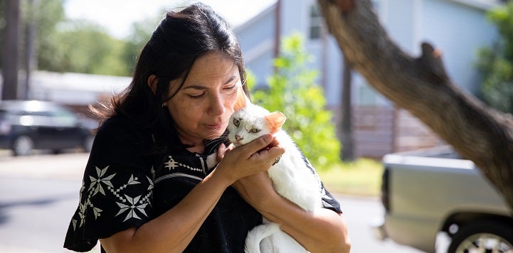 Woman with long hair in black top hugging white kitten 