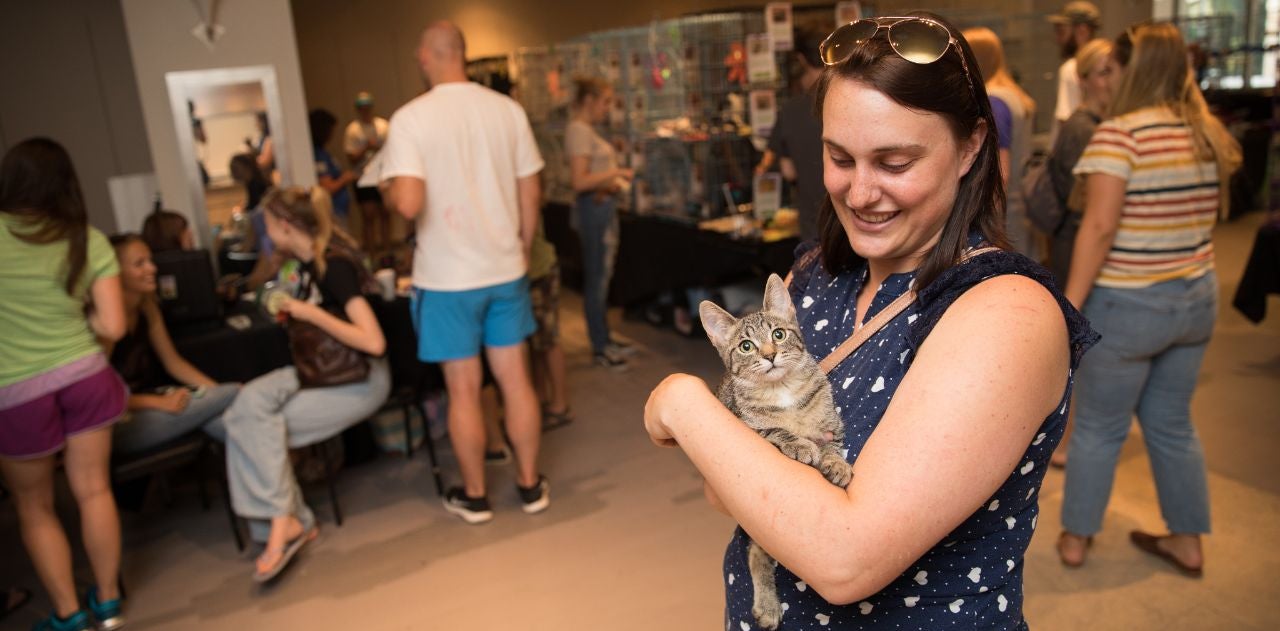 Woman holding a tabby cat while standing in an adoption center during an event