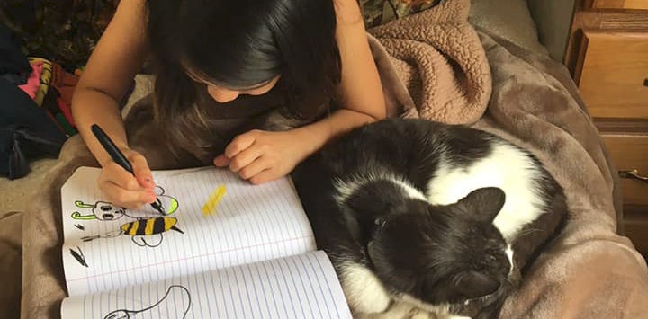 Black and white cat curled up next to little girl with dark hair writing