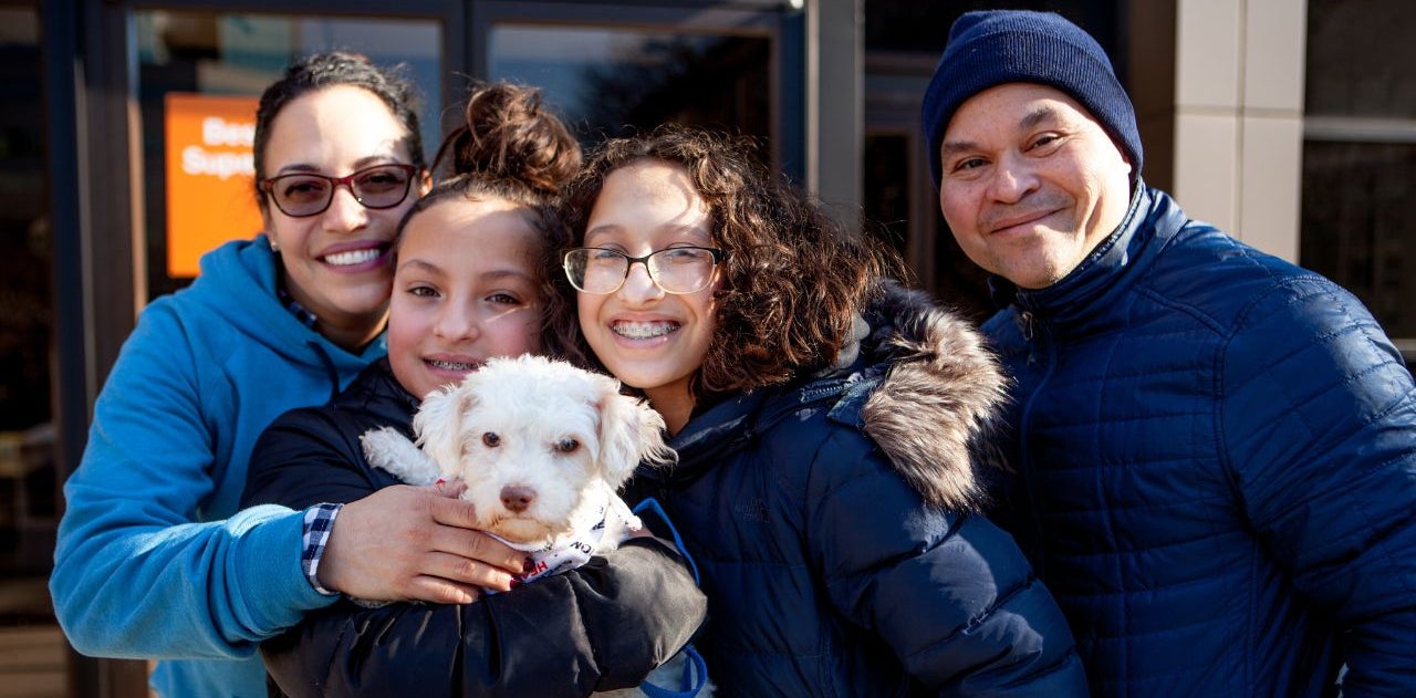 A family of four people holds a small white dog at an adoption event