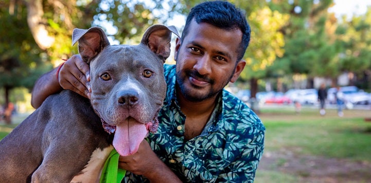 Man in teal multi colored shirt sitting with dark gray pit bull type dog